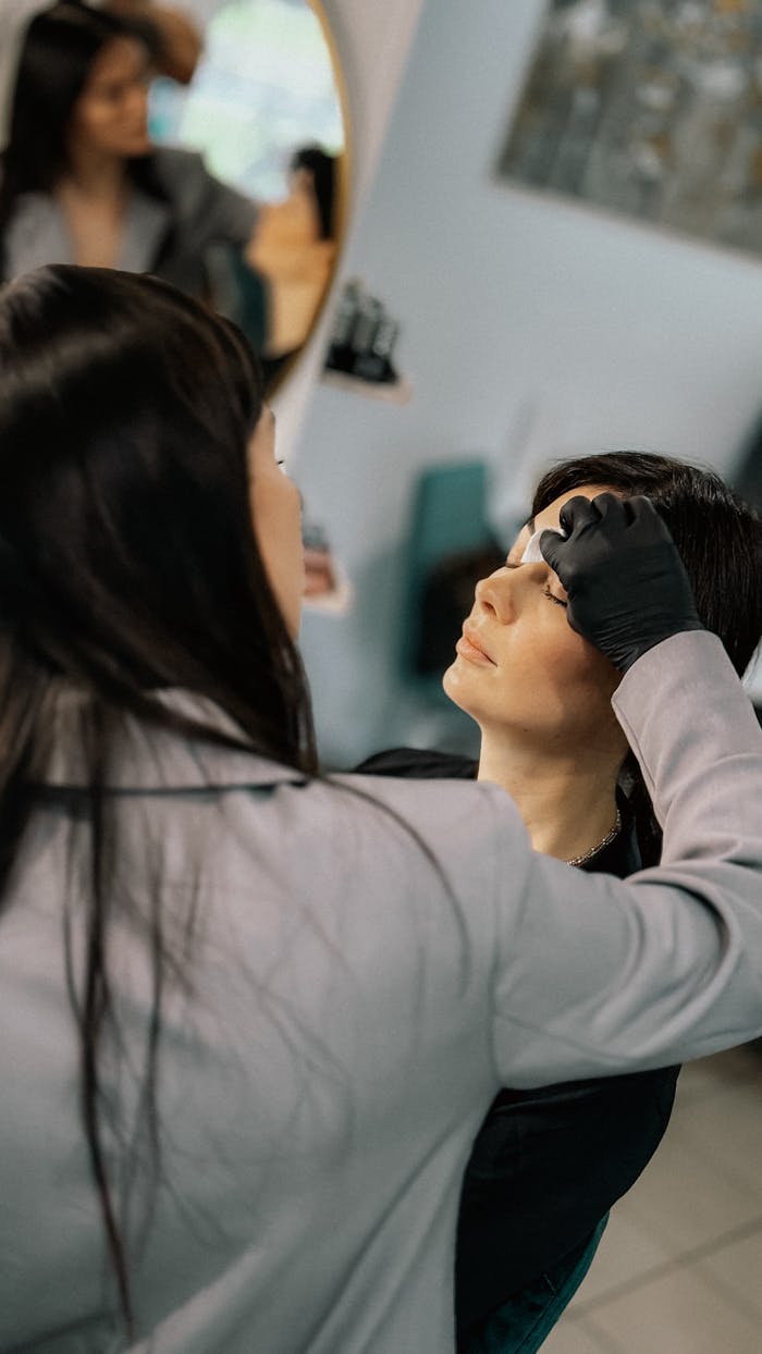our-experience Makeup artist carefully applying eyebrow makeup to client in a salon.